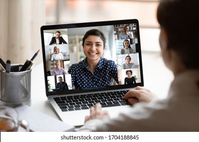 Woman sit at desk looking at computer screen where collage of diverse people webcam view. Indian ethnicity young woman lead video call distant chat, group of different mates using videoconference app