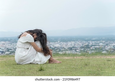 Woman Sit Facing Side Face Down Knee On Grass At Top Mountian Sky ,city And Nature View Background. Feel Sad And Depress.