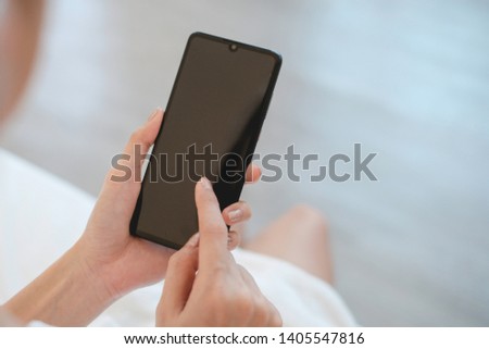 Woman sit on the bed and holding blank screen smartphone after shower, technology concept.