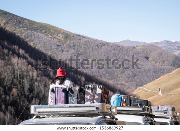 Woman sit on car rooftop with suitcase to see\
a beautiful view while traveling in Caucasus Mountains ,Georgia.\
The new natural landmark for\
tourist