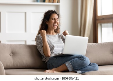 Woman sit on sofa put pc on lap clenched fists scream with joy while read great news on laptop. Gambler celebrate online auction bet victory. Got incredible offer sincere emotions of happiness concept