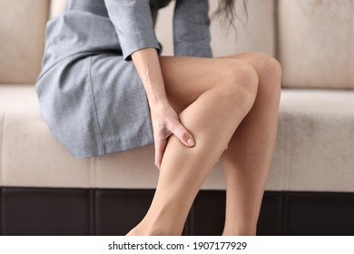 Woman siting on couch and holding shin with her hand closeup. Prevention of varicose veins concept
