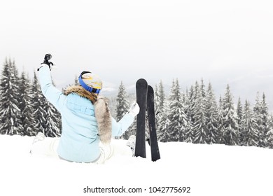 Woman Siting On Snow And Makes Selfie From Go Pro   With Ski Blades On Mountain In Forest In Winter Time