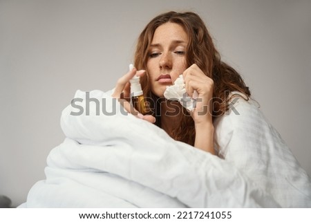 Woman sits in bed and treats runny nose with nasal spray