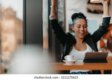 A Woman Sits In A Cafe With Her Arms Raised And Celebrating A Job Well Done.Business Concept