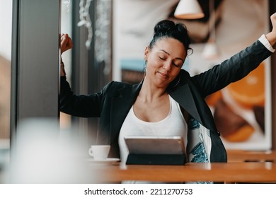 A Woman Sits In A Cafe With Her Arms Raised And Celebrating A Job Well Done.Business Concept