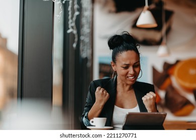 A Woman Sits In A Cafe With Her Arms Raised And Celebrating A Job Well Done.Business Concept