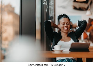 A Woman Sits In A Cafe With Her Arms Raised And Celebrating A Job Well Done.Business Concept