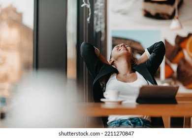 A Woman Sits In A Cafe With Her Arms Raised And Celebrating A Job Well Done.Business Concept