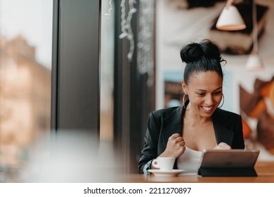 A Woman Sits In A Cafe With Her Arms Raised And Celebrating A Job Well Done.Business Concept