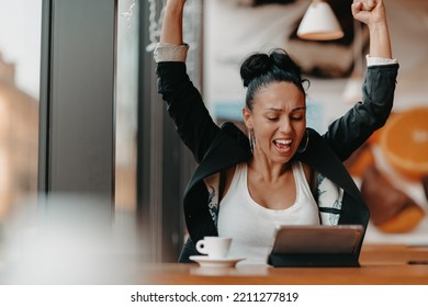 A Woman Sits In A Cafe With Her Arms Raised And Celebrating A Job Well Done.Business Concept