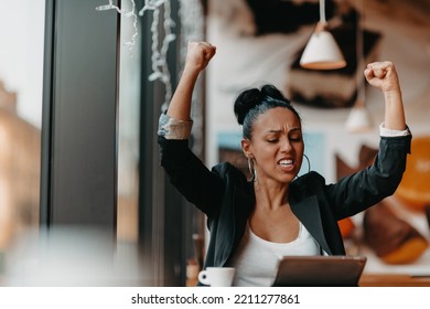 A Woman Sits In A Cafe With Her Arms Raised And Celebrating A Job Well Done.Business Concept