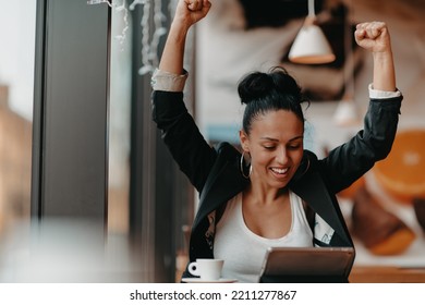 A Woman Sits In A Cafe With Her Arms Raised And Celebrating A Job Well Done.Business Concept