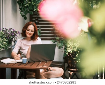 A woman sits comfortably with a laptop, engaged in work surrounded by lush home gardening - Powered by Shutterstock