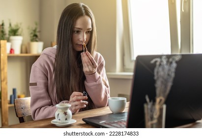Woman sits in front of a computer screen and sniffs essential oil from a bottle to relax and restore energy or for distance learning on oils and meditation session.