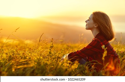 Woman sits with her back in the field and admires the sunset in the mountains - Shutterstock ID 1022465209