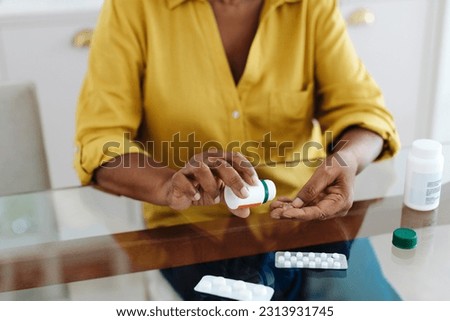 Woman sits at her table taking medication to manage her chronic disease. Senior woman following a strict treatment regimen to maintain her health, taking measures to keep her condition under control.