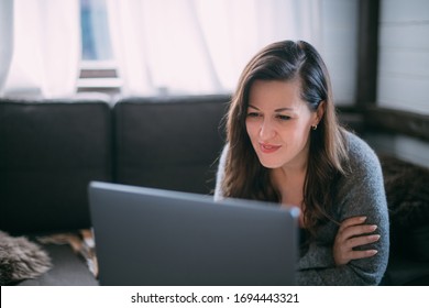 A Woman Sits In The Living Room With A Laptop, Looks At The Screen, Takes Notes, Learns A Foreign Language, Reads An Online Training Course, Education On The Internet, Consults With A Client On Video