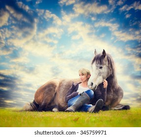 woman sits at lying horse and looking outside over pasture and sky background