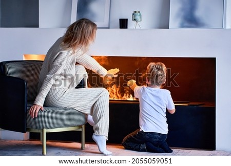 Woman sits near fireplace with little boy in living room.