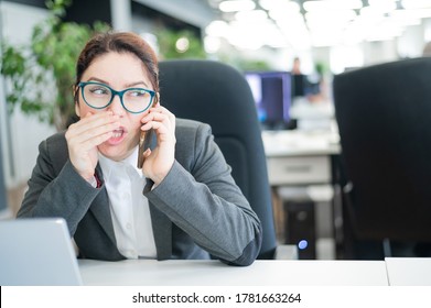 A woman sits in an office at her desk and gossips on the phone. Corporate ethics. Female employee in a suit tells secrets on a smartphone at work.