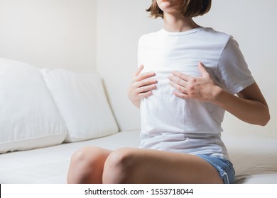 Woman sits on a bed and holds her breasts. Concept of breast pain, breast cancer awareness or menstrual pain