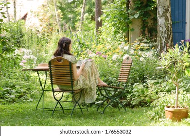 A Woman Sits On A Chair In A Garden.