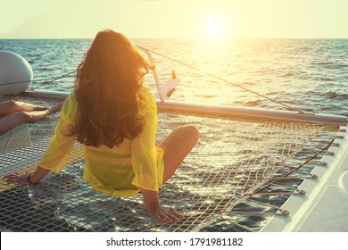 Woman sits on the deck of a sailing catamaran at sunset in the sun. Rear view of a woman enjoying the azure water on the deck of a sailing yacht. Selective focus, blur