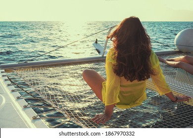 Woman sits on the deck of a sailing catamaran at sunset in the sun. Rear view of a woman enjoying the azure water on the deck of a sailing yacht. Selective focus, blur