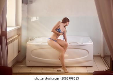 Woman sits on edge of hot hydromassage tub and touches water with her hand.
