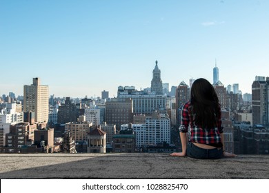 A Woman Sits On The Edge Of A Rooftop And Watches Over The New York City Skyline.