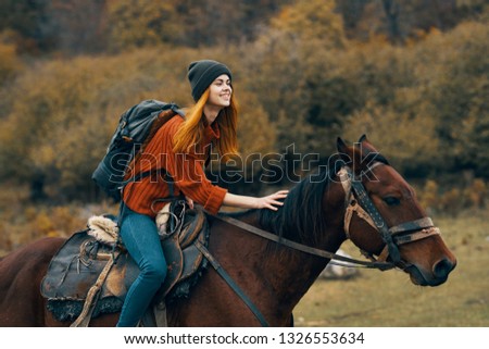 woman sits on a horse on the nature of the meadow and a backpack on the back               