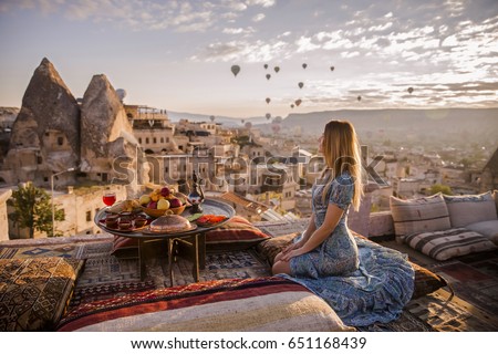 A woman sits on one of the Cappadocia roof in early morning sunrise, when balloons fly. Romantic scene Cappadocia, Turkey.