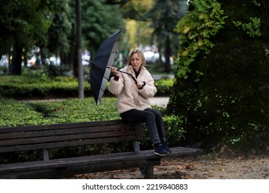 A Woman Sits On A Park Bench. An Umbrella Broke Down In Rainy Weather.