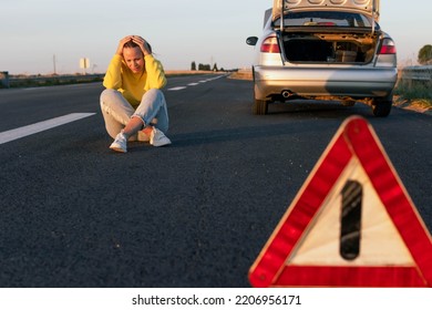 A Woman Sits On The Pavement Near A Broken Car, Upset, Worries Next To It Is A White-red Emergency Stop Sign. The Girl Is Waiting For Help With A Broken Car, There Is A Place For An Inscription