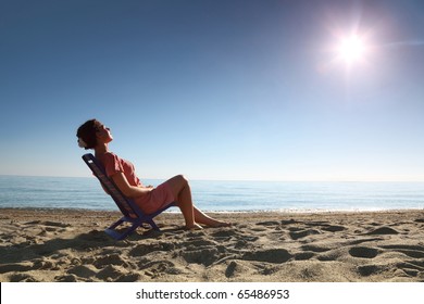 Woman sits on  plastic chair on  sea-shore by  person to  sun and becomes tanned, heaving up  head
