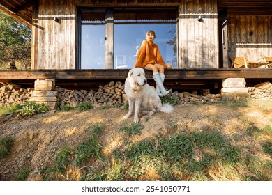 A woman sits on the porch of a rustic cabin, enjoying the early sun, while her loyal white dog stays close by. A cozy, serene start to a day in nature's embrace - Powered by Shutterstock