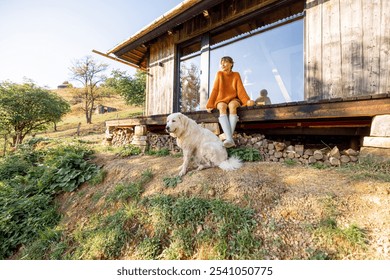 A woman sits on the porch of a rustic cabin, enjoying the early sun, while her loyal white dog stays close by. A cozy, serene start to a day in nature's embrace - Powered by Shutterstock