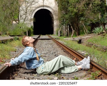 A Woman Sits On A Railroad Track. Woman Sitting On The Sleepers Of An Old Railroad.