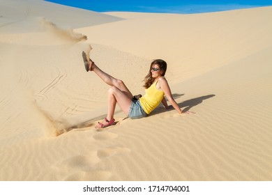 Woman sits on the sand in the desert, wearing a T-shirt and shorts