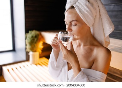 Woman Sits On Spa In A Sauna Resting. Hot Steam Relaxation. Skin Detox Therapy. Enjoy The Warm Air. The Girl Drinks Mineral Water.Drinking Clean Water In The Sauna. Dehydration. Herbal White Tea