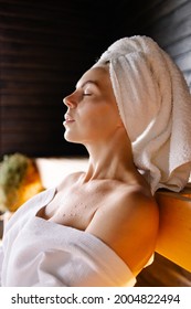 Woman Sits On A Spa In A Sauna Resting Procedure. Hot Steam Relaxation. Sweaty Skin Detox Therapy. Enjoy The Warm Air. Pleasure Towel On Head. Clean Health Skin. Welness Lifestyle