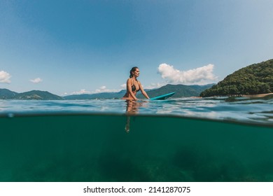  woman sits on the surfboard in the ocean,  with underwater view - Powered by Shutterstock