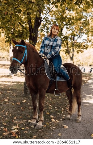 A woman sits on top of a horse. Horse riding in the autumn park. High quality photo