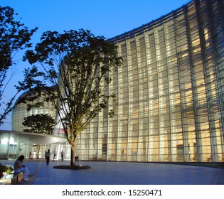 Woman Sits Outside Modern Glass Museum In Early Evening