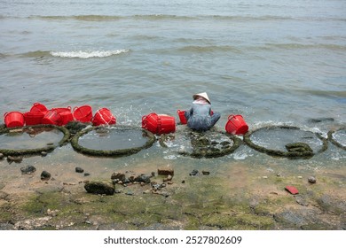 A woman sits washing fish baskets after the fish market on the beach, in a small fishing village in Binh Thuan, Vietnam - Powered by Shutterstock