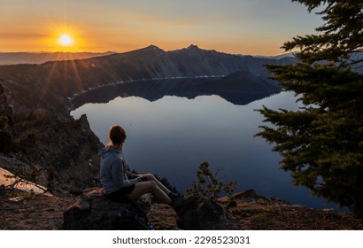 Mujer sentada para ver la puesta de sol sobre el lago Crater en verano desde el sendero de Garfield