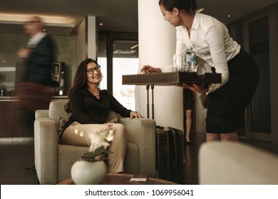 Woman Sitting At Airport Lounge With Waitress Serving Coffee. Business Traveler At Airport Waiting Lounge.