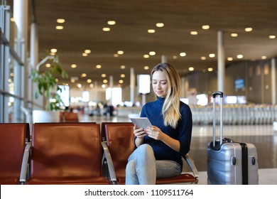 Woman sitting in airport waiting room with valise and using tablet. Concept of modern technology and traveling. - Powered by Shutterstock