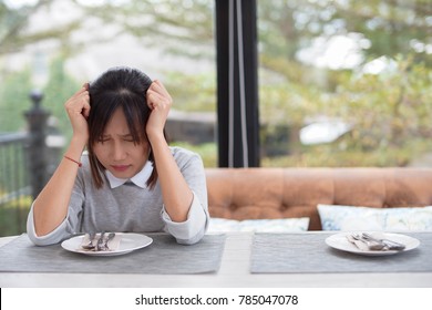 Woman sitting alone at dining table getting stressful and headache due to anorexia disorder